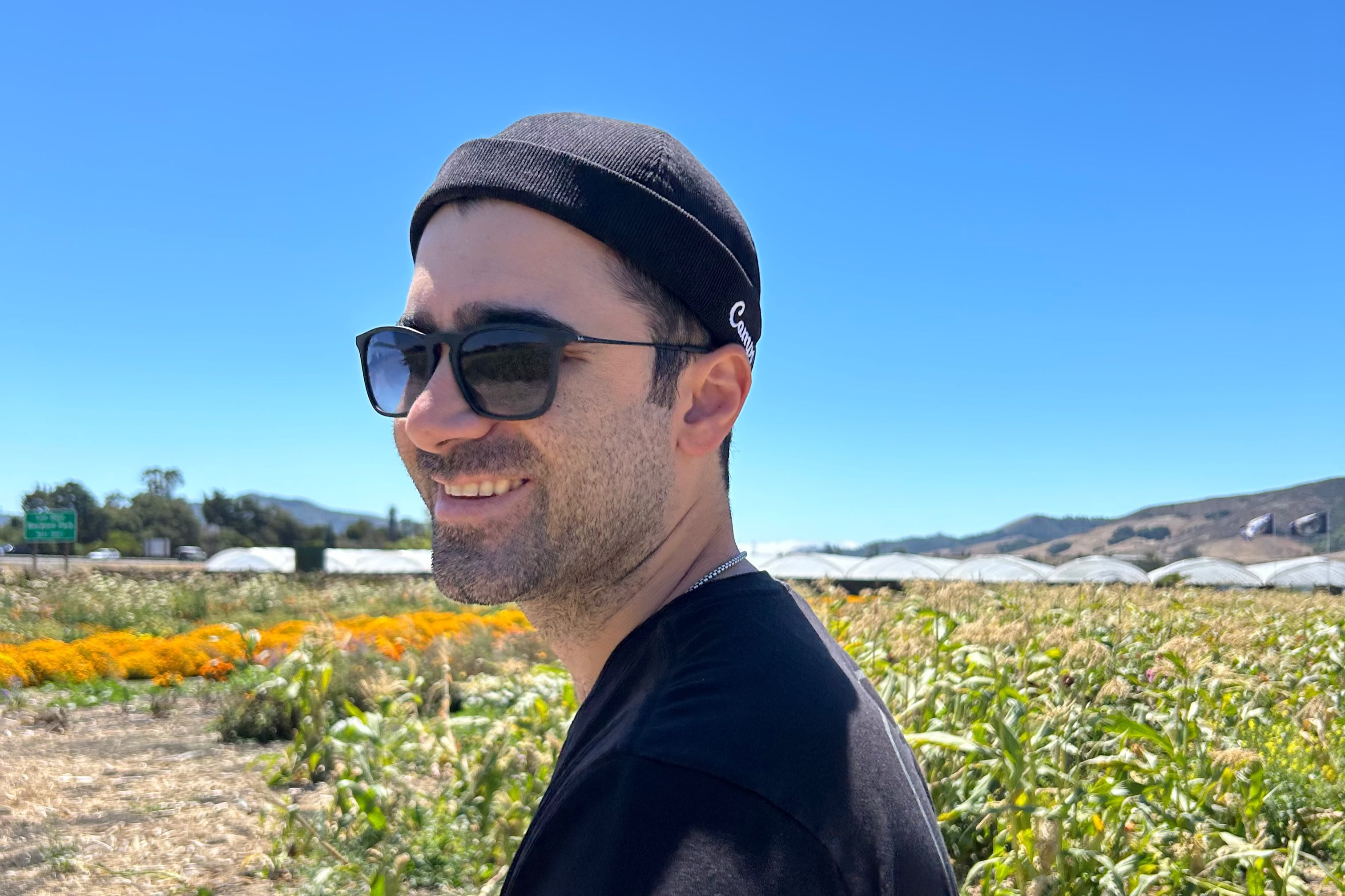 Man wearing sunglasses and a black beanie standing in a field with clear blue sky