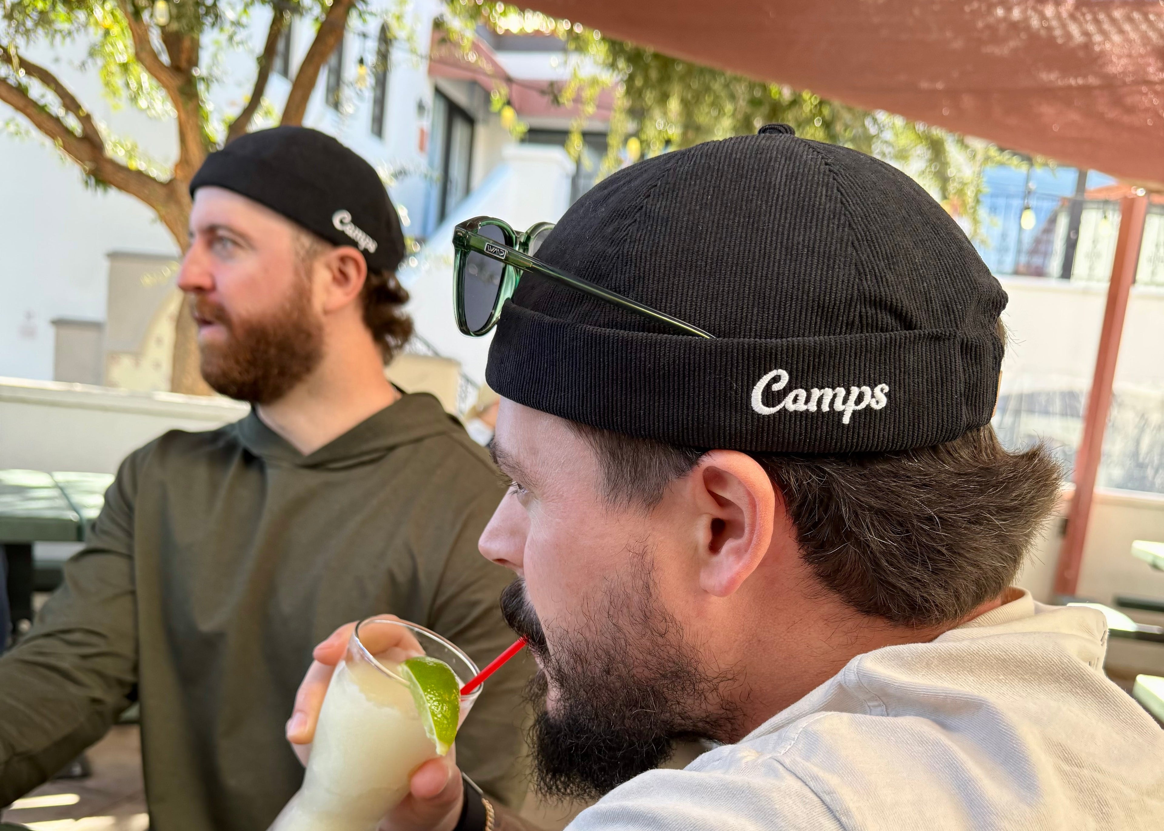 Two men sitting outdoors, one drinking a beverage, with a casual setting.