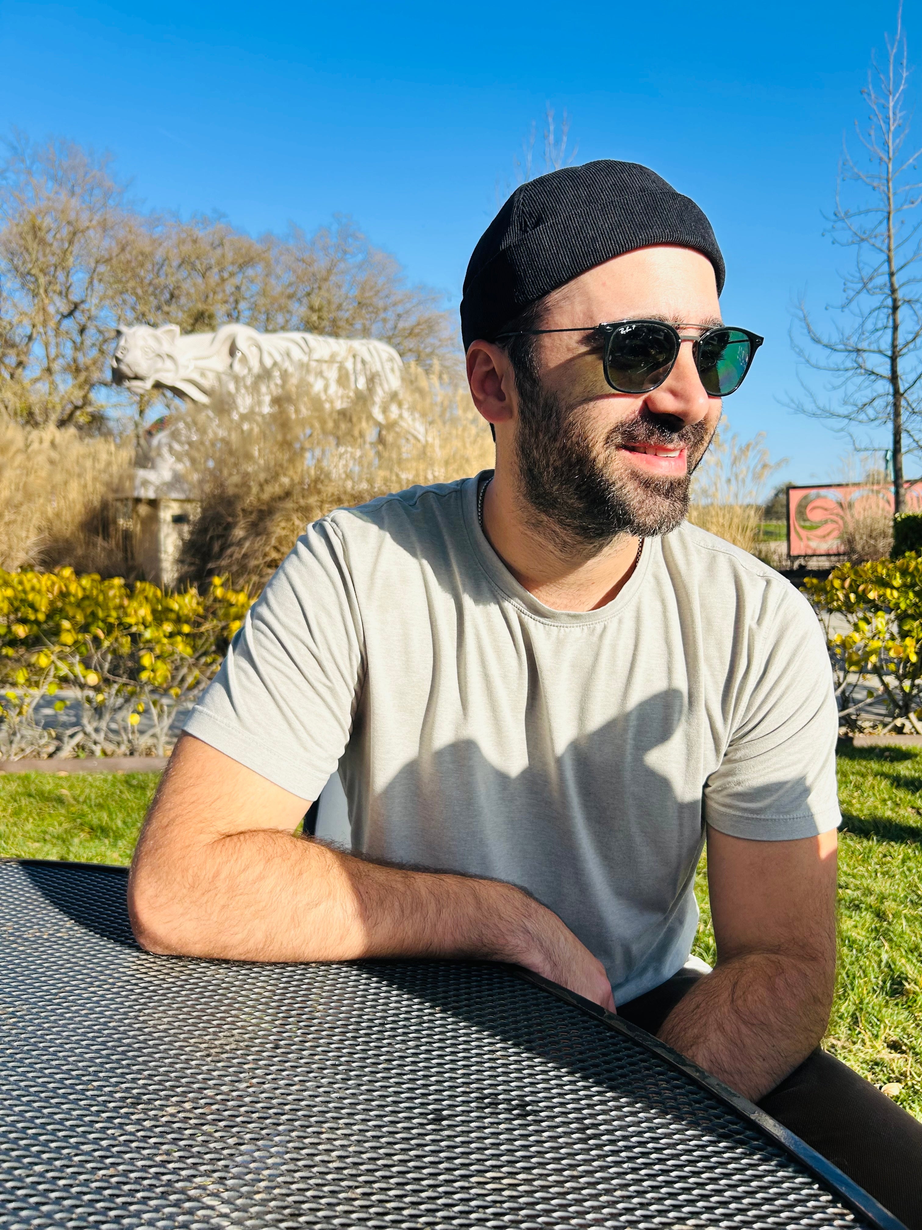 Man wearing sunglasses and a docker cap sitting outdoors with a scenic background