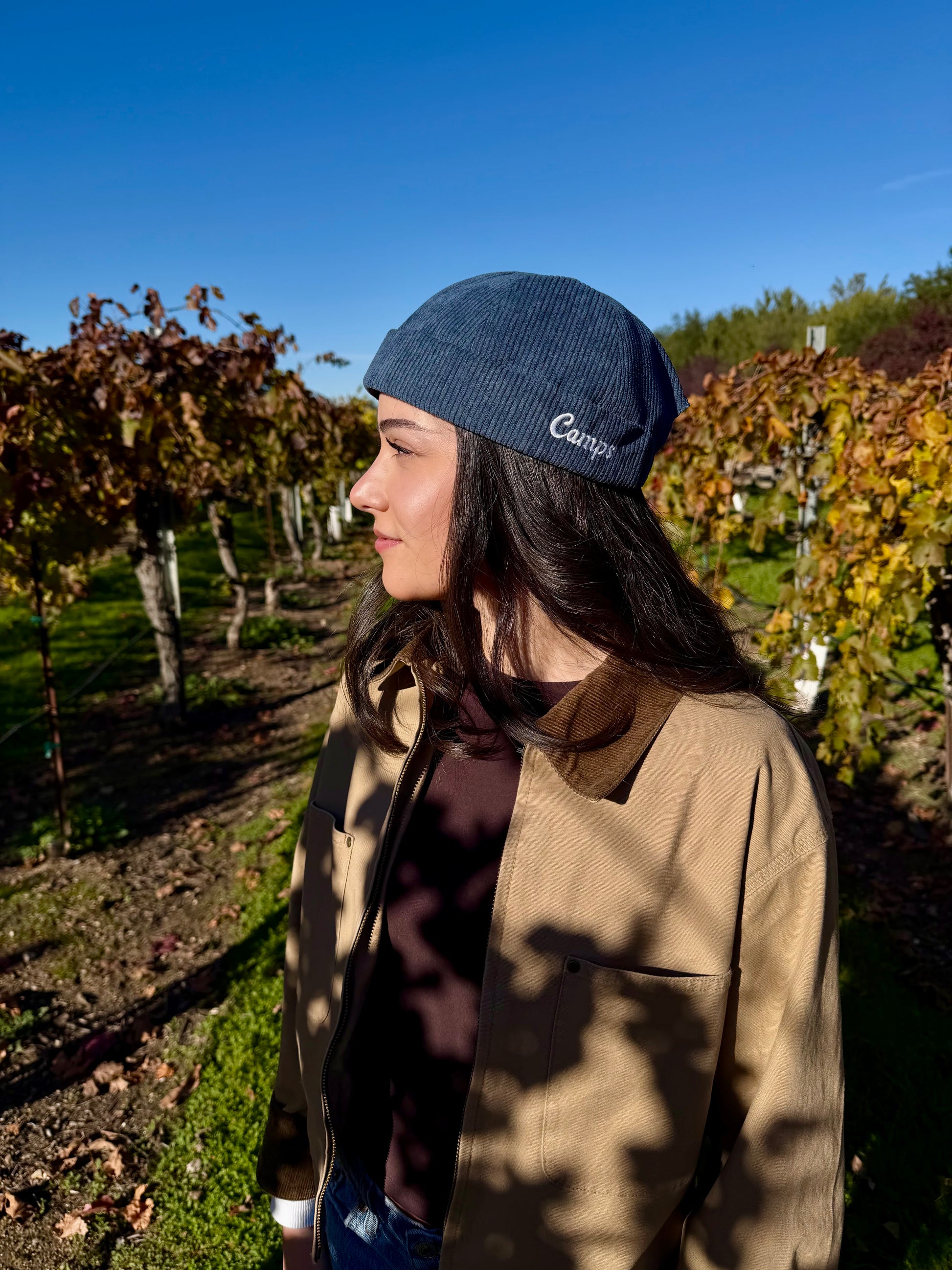 Woman wearing a blue brimless cap with 'Camps' logo in a vineyard setting